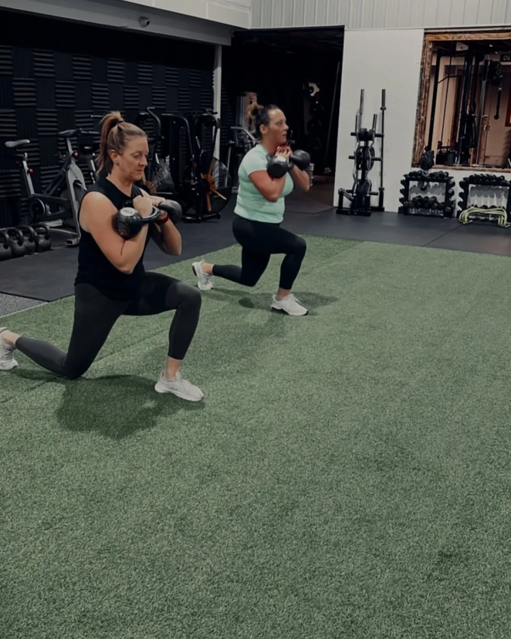 Adult members kettlebell squatting on the turf during a group session